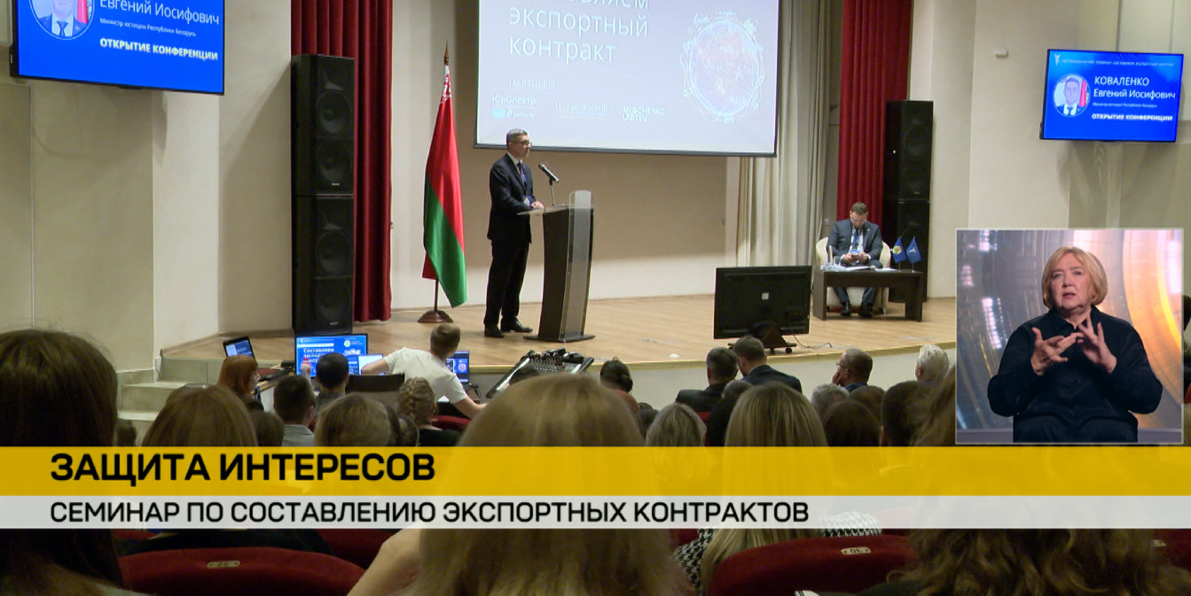 Зал заполнен слушателями, которые сидят в креслах спиной к камере и смотрят в сторону сцены