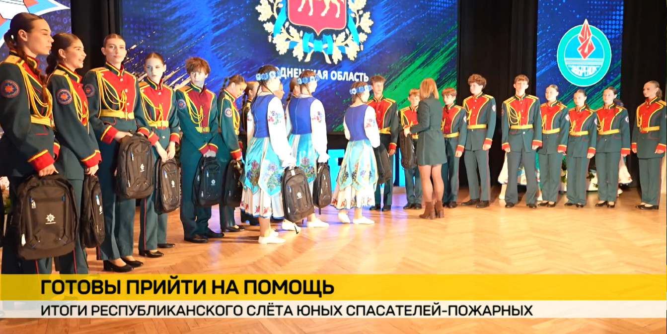 Слёт юных спасателей-пожарных: награждение участников на сцене Гродненской области. Подростки в парадной форме МЧС и народных костюмах стоят в шеренге и держат черные рюкзаки.