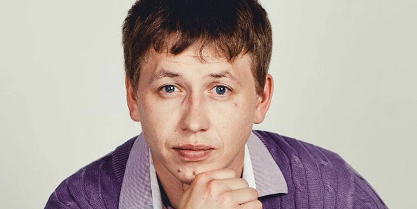 Портрет актера Владимира Курочкина в фиолетовом кардигане, подпирающего подбородок рукой.