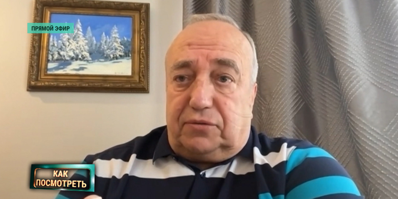 Франц Клинцевич жестикулирует во время прямого эфира программы «Как посмотреть». Сзади висит картина с зимним лесом, в левом нижнем углу экрана — логотип передачи.