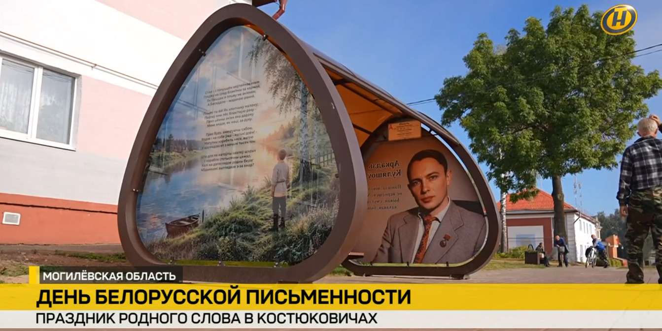 Автобусная остановка в Костюковичах в форме открытой книги, украшенная портретом Алеся Письменкова и его стихами к Дню белорусской письменности. На переднем плане — репортажная плашка ONT.